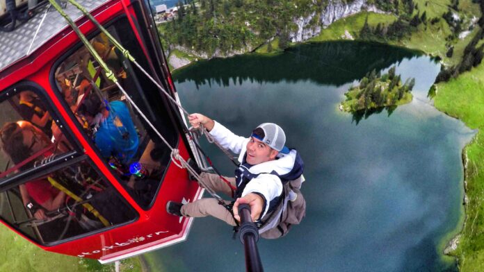 011 Devin Super Tramp 10 Devin hanging outside of a gondola over a lake, shooting with a selfie-stick