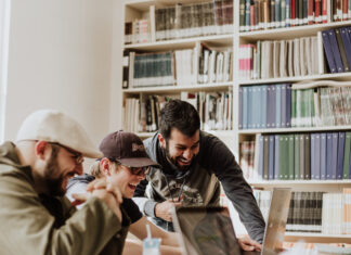 Why every Twitch streamer should join a Twitch Team Several young men all part of a Twitch Team, are gathered and smiling at a table with laptops on it